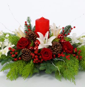 This stunning design is composed of red roses paired with white lily and orchids that are donned in red Hypericum berries, red ornamental balls and pine cones, all nestled into a bed of Christmas greens. 