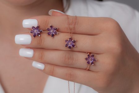 The young woman in a white dress and with a white nail polish hand shows the ring, necklace and earrings in the shape of a purple lotus flower in rose color.